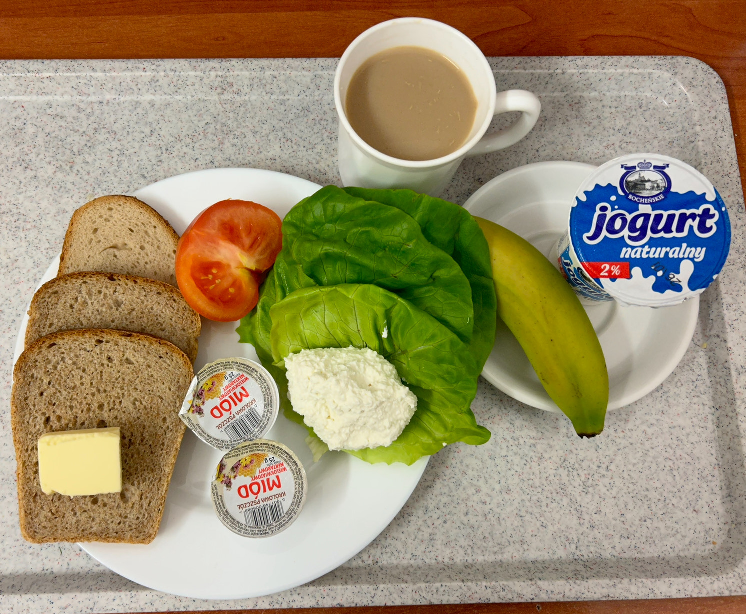 Na zdjęciu znajduje się: Jogurt naturalny, Kawa zbożowa z mlekiem, Chleb mieszany pszenno-żytni, Chleb Graham, Masło extra 82%, Twarożek, Miód, Banan, Sałata zielona, Pomidor